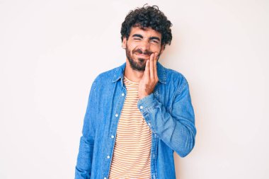 Kıvırcık saçlı ve ayı gibi giyinmiş yakışıklı genç adam diş ağrısı ya da diş hastalığından dolayı acı dolu bir ifadeyle dudaklarına dokunuyor. dişçi 