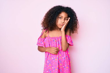 Kıvırcık saçlı Afro-Amerikalı çocuk sıradan giyinmiş, yorgun görünüyor ve kollarını kavuşturarak depresyondan sıkılmış görünüyor.. 