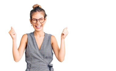 Sarı saçlı, iş kıyafetleri ve gözlük takan güzel beyaz kadın kollarını kaldırarak ve açık gözlerle başarıyı kutluyor ve şaşırıyor. Kazanan konsept. 