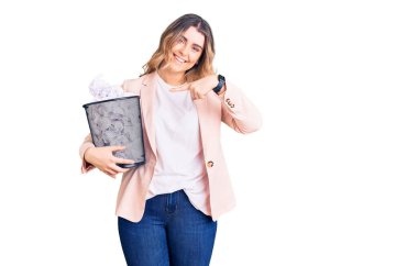 Kırışmış kağıtlarla dolu kağıt kutusunu tutan beyaz bir kadın mutlu bir şekilde eli ve parmağı ile işaret ediyor. 