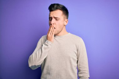 Mor izole arka plan üzerine günlük süveter giyen yakışıklı beyaz bir adam ağzıyla esnemekten sıkılmış. Huzursuz ve uykulu..