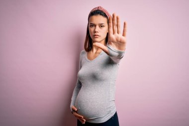 Genç, güzel, hamile bir kız pembe arka planda bebek bekliyor ve avucunun içi gibi şarkı söylemeyi kesiyor. Yüzünde olumsuz ve ciddi bir jest olan uyarı ifadesi.