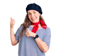 Fransız bereli ve çizgili tişörtlü genç, güzel sarışın kadın. Arka tarafı işaret ediyor. El ve baş parmakları havada, kendinden emin. 