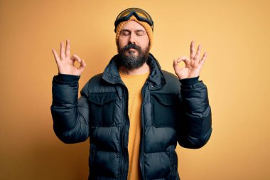 Sakallı, kar maskesi takmış, kar maskesi takmış, kar maskesi takmış, gözleri kapalı, meditasyon yaparken parmaklarıyla gülümseyen yakışıklı, kel bir kayakçı. Yoga konsepti.