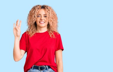 Kıvırcık saçlı, sıradan kırmızı tişörtlü, dört numaralı parmaklarıyla işaret eden, kendinden emin ve mutlu gülümseyen genç sarışın kadın.. 