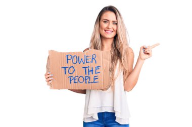 Genç, güzel sarışın kadın elinde güç, mukavva pankartlara sarılıp gülümsüyor, mutlu bir şekilde elini ve parmağını yana doğru gösteriyor. 