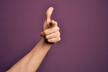 İzole edilmiş mor arka planda parmaklarını gösteren, kamerayı işaret eden ve yönü gösteren beyaz bir gencin eli.