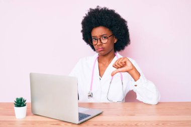 Doktor steteskobu takan Afro-Amerikalı genç bir kadın kızgın yüzlü bir bilgisayar dizüstü bilgisayar kullanıyor, olumsuz işaretler baş parmakları reddetmeyi, reddedilmeyi gösteriyor. 