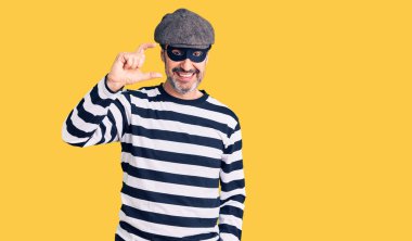 Orta yaşlı, hırsız maskesi takan, gülümseyen, kendine güvenen, el hareketleriyle hareket eden, parmaklarıyla işaret yapan ve kameraya bakan yakışıklı bir adam. ölçüm kavramı. 