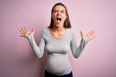 Genç, güzel bir kız hamile, pembe arka planda bebek bekliyor. Başarılı olmak için çıldırıyor ve çıldırıyor. Kolları kalkık ve gözleri kapalı, heyecanlı bir şekilde bağırıyor. Kazanan konsept
