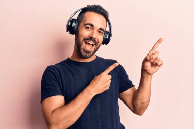 Genç İspanyol adam müzik dinliyor kulaklık takıyor gülümsüyor ve kameraya bakıyor iki eliyle ve parmaklarıyla kenarı işaret ediyor.. 