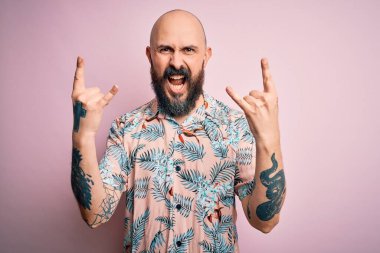 Sakallı ve dövmeli yakışıklı, pembe arka planda sıradan bir çiçek gömleği giyen, çılgın bir ifadeyle elleri havada rock sembolü yapan kel bir adam. Müzik yıldızı. Ağır müzik konsepti.