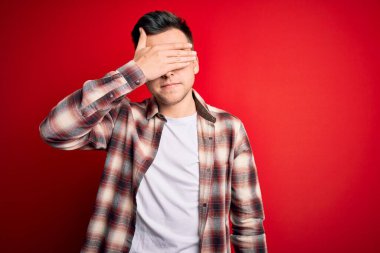 Kırmızı izole arka plan üzerine gündelik modern tişört giyen yakışıklı beyaz bir adam. Gözleri elle kapatıyor, ciddi ve üzgün görünüyor. Görme, saklama ve reddetme konsepti