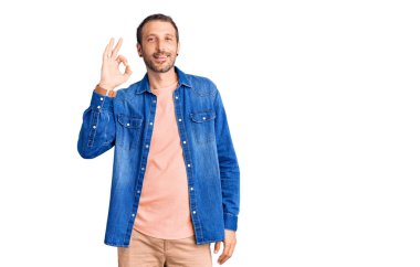 Gündelik kıyafetler giyen, gülümseyen, el ve parmaklarıyla imza atan yakışıklı bir genç. başarılı ifade. 