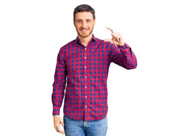 Ayılı yakışıklı genç adam rahat bir tişört giyiyor gülümsüyor ve el hareketleriyle el hareketi yapıyor parmaklarıyla işaret yapıyor ve kameraya bakıyor. ölçüm kavramı. 