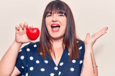 Zaferi kutlayan kalbi tutan genç ve iri bir kadın. Mutlu bir gülümseme ve kaldırılmış ellerle kazanan bir ifade. 