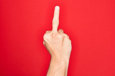 Hand of caucasian young man showing fingers over isolated red background showing provocative and rude gesture doing fuck you symbol with middle finger