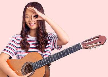 Genç güzel Çinli kız klasik gitar çalıyor gülümsüyor mutlu bir şekilde el pençe divan duruyor. 