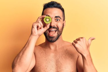 Genç İspanyol üstsüz bir adam elinde kivi, baş parmağını kaldırmış, ağzı açık gülümsüyor. 