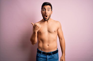 Genç, yakışıklı, sakalsız, pembe arka planda duran güçlü bir adam. Elle işaret ederek şaşırmış, ağzı açık, şaşkın bir ifadeyle..