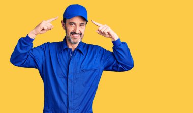 Orta yaşlı, yakışıklı, tamirci üniforması giyen, gülümseyen, iki eliyle kafasını gösteren, harika bir fikir ya da düşünce, iyi bir hafıza. 