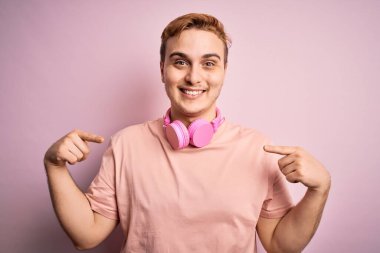 Genç, kızıl saçlı, müzik dinleyen, pembe arka planda kulaklık takan, kendine güvenen, gülümseyen, kendini gururlu ve mutlu gösteren bir adam..