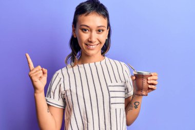 İçen genç kadın gülümsüyor. Mutlu bir şekilde işaret ediyor. El ve parmak yanda. 