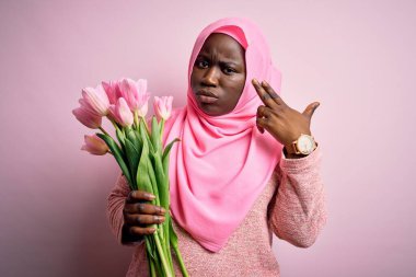 Genç Afro-Amerikan artı cüsseli kadın elinde pembe lale buketi tutarak kendini ve parmaklarını silah gibi doğrultarak vuruyor, intihar jesti.