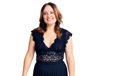 Zarif bir elbise giyen güzel beyaz bir kadın pozitif ve mutlu görünüyor ve kendine güvenen bir gülümsemeyle dişlerini gösteriyor. 