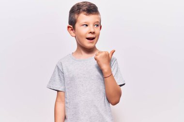 Hoş sarışın çocuk, günlük kıyafetler giyiyor, gülümsüyor, gülümsüyor ve başparmağıyla yan tarafı işaret ediyor.. 