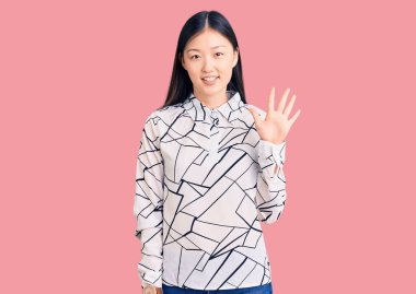 Genç, güzel, Çinli bir kadın, gündelik tişörtler giyip beş numarayı gösterirken, mutlu ve kendinden emin bir şekilde gülümsüyor.. 