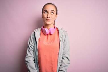 Güzel, sportif bir kadın spor yapıyor, müzik dinliyor, pembe arka planda kulaklık takıyor, gülümsüyor ve diğer tarafa bakıyor ve düşünüyor..