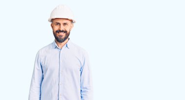 Yüzünde mutlu ve havalı bir gülümseme olan mimar şapkası takan genç yakışıklı bir adam. şanslı kişi. 