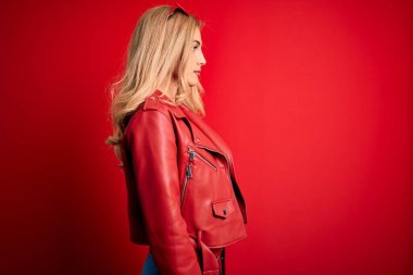 Genç, sarışın, sıradan bir ceket giyen, kırmızı arka planda duran, kendine güvenen, doğal yüzlü, rahat bir poz veren, kendine güvenen bir kadın..