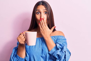 Genç, güzel esmer kadın bir kupa kahve içiyor. Ağzını eliyle kapatıyor. Şok geçiriyor ve hata yapmaktan korkuyor. şaşırmış ifade 