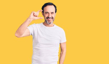 Orta yaşlı, yakışıklı, sıradan tişörtler giyen, gülümseyen, kendine güvenen, el hareketi yapan, parmaklarıyla işaret yapan ve kameraya bakan bir adam. ölçüm kavramı. 