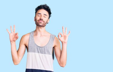 Günlük kıyafetler giyen genç İspanyol adam rahatla ve gözleri kapalı gülümse parmaklarıyla meditasyon hareketi yapıyor. yoga konsepti. 