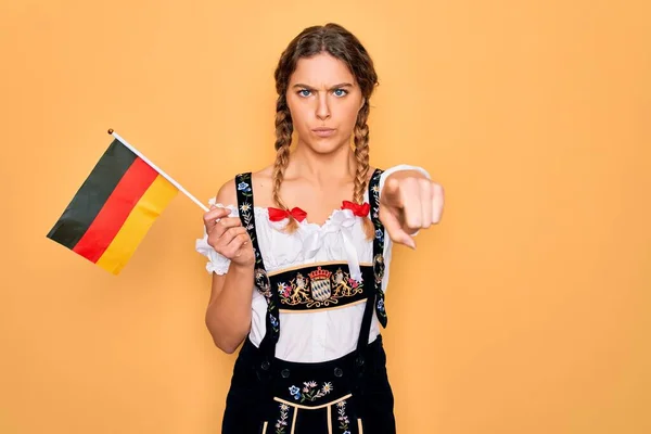美丽的金发爱国女人 蓝眼睛 身穿十月盛装 手持德国国旗 手指指向摄像机和你 正面是积极自信的姿态 — 图库照片