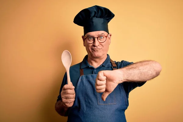 앞치마를 모자를 배경에 얼굴로 숟가락을 중년의 요리사 엄지손가락을 아래로 내리는 — 스톡 사진