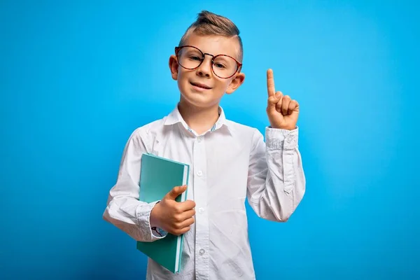 小さな白人の学生の子供はスマートグラスを身に着けていると学校から本を持っている幸せな顔を持つアイデアや質問指差し指で驚いて ナンバーワン — ストック写真