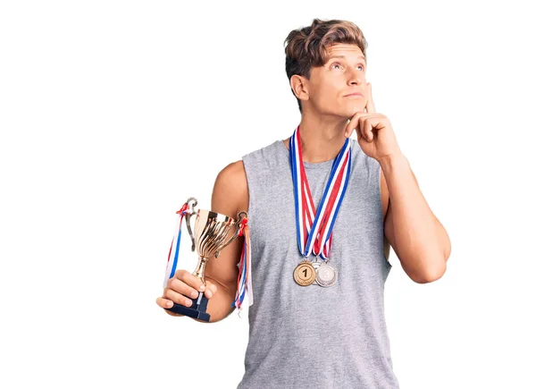 Joven Hombre Guapo Sosteniendo Trofeo Campeón Usando Medallas Cara Seria —  Fotos de Stock