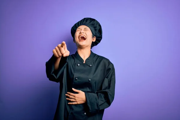 年轻美丽的中国厨师女士穿着炊具制服 头戴紫色背景的帽子 笑着看着你 用手指对着镜头 满身羞愧的表情 — 图库照片