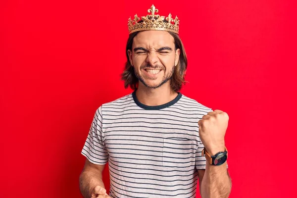 Young handsome man wearing prince crown celebrating surprised and amazed for success with arms raised and eyes closed