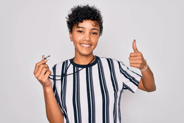 Young beautiful african american afro referee woman wearing striped uniform using whistle happy with big smile doing ok sign, thumb up with fingers, excellent sign