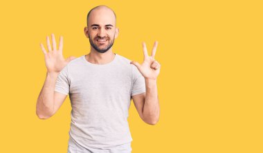 Gündelik tişört giyen genç ve yakışıklı bir adam 8 numaralı parmaklarıyla onu gösterirken kendinden emin ve mutlu bir şekilde gülümsüyor.. 