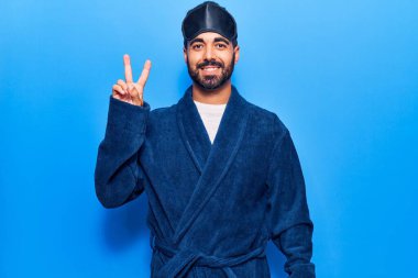 Uyku maskesi takan ve gülümseyen neşeli yüzüyle gülümseyen genç İspanyol adam zafer işareti yapıyor. İki numara.. 