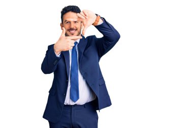 İş kıyafetleri giymiş, gülümseyen genç İspanyol adam ellerle ve mutlu yüzle çerçeve yapıyor. yaratıcılık ve fotoğrafçılık kavramı. 