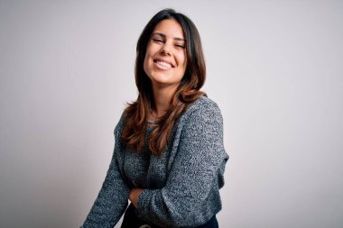 Genç ve güzel esmer kadın mutlu ve kendinden emin gülümsüyor. Yüzünde tebessümle dikilip, izole beyaz arka planda günlük süveter giyiyorsun.