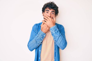 Kıvırcık saçlı ve sıradan kot ceket giyen yakışıklı genç adam ağzını yanlışlıkla ellerle kapatmış. gizli kavram. 