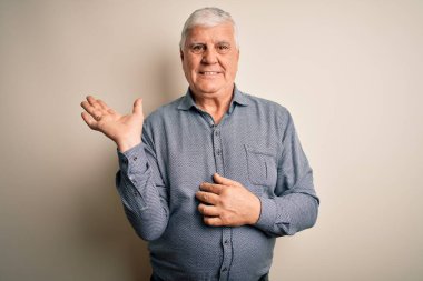Kıdemli yakışıklı beyaz gömlekli adam izole edilmiş beyaz arka planda dikiliyor neşeli bir şekilde gülümsüyor ve avuç içi kameraya bakıyor..